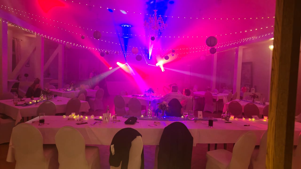 Derselbe Festsaal am Abend mit farbiger Lichtshow, Nebel und feiernden Gästen